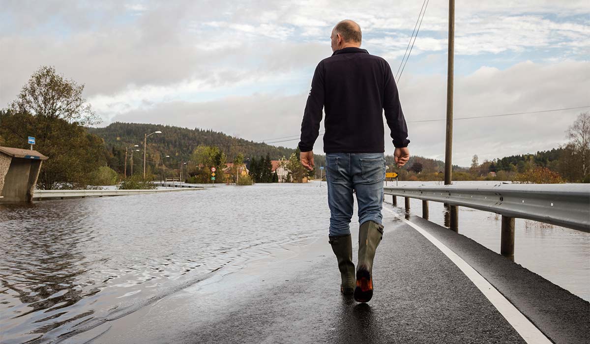 Mann med gummistøvler går på flomrammet vei